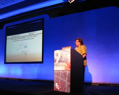 Paola Chiaramonte parla dal podio del congresso ESLO di Londra, sullo schermo una diapositiva sul torque dei denti