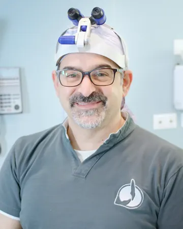 Il Dott. Piero Recchia sorride, con la lampada frontale e la polo dello studio, nella sala chirurgica
