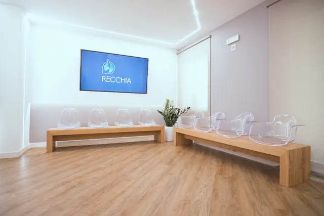 La sala d'attesa con le panche di rovere massiccio, le sedie trasparenti e lo schermo col marchio
