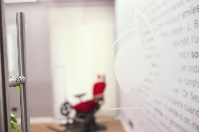 La porta di vetro con le frasi sul sorriso e, dietro, la poltrona da dentista d'epoca in velluto rosso
